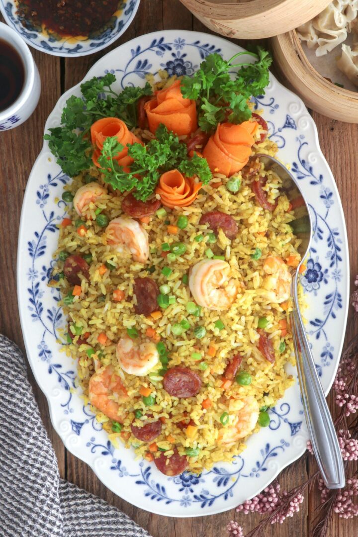 Yang Chow fried rice in a serving platter loaded with shrimp, sausages, eggs, carrots, and green peas.
